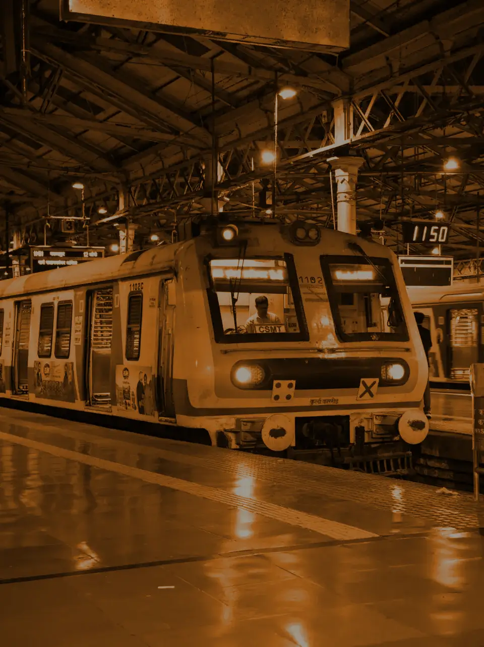 A local train waiting at a lit platform, the station clock reading 11:50