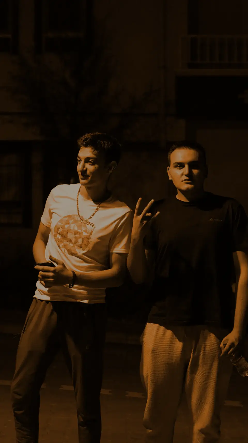 Two friends posing at night, one in a white tee